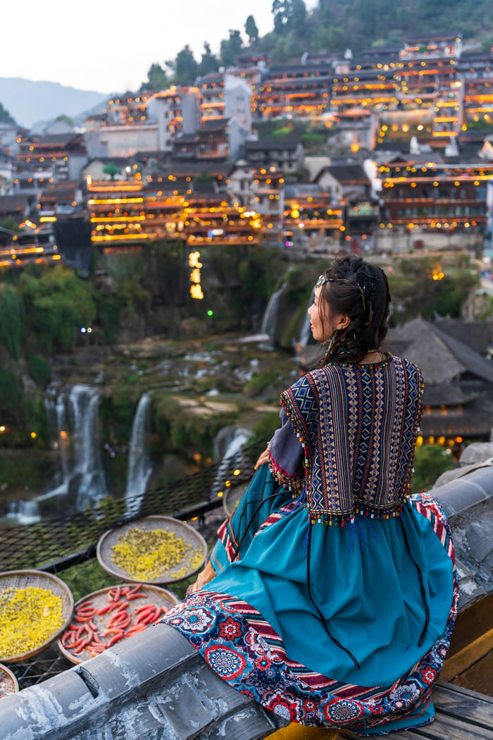 Mujer sentada con comida al lado apreciando de un paisaje de algunas casas de la ciudad de Lijiang.