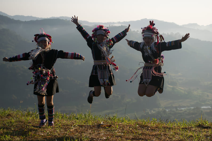 3 personas vestidas con una vestimenta típica saltando para una foto con un paisaje de montaña de fondo.